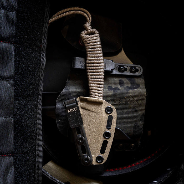 TRAIL GOAT knife in coy/olv color with paracord handle, secured in a tactical sheath on a camo background.