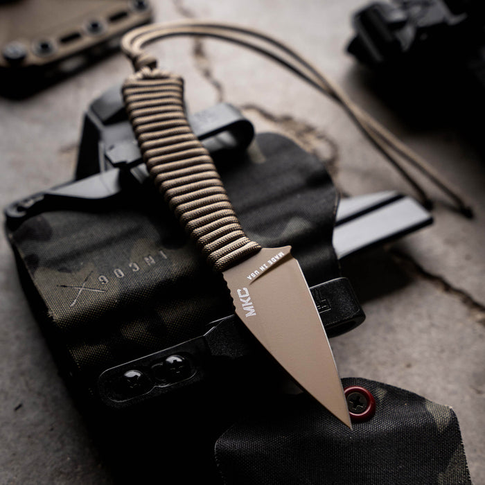 TRAIL GOAT knife with a coy/olive drab handle resting on tactical gear, showcasing its rugged design for outdoor use.