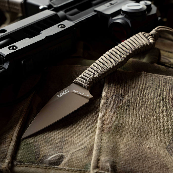 TRAIL GOAT knife with a coy/olive drab handle, resting on tactical gear alongside a firearm.