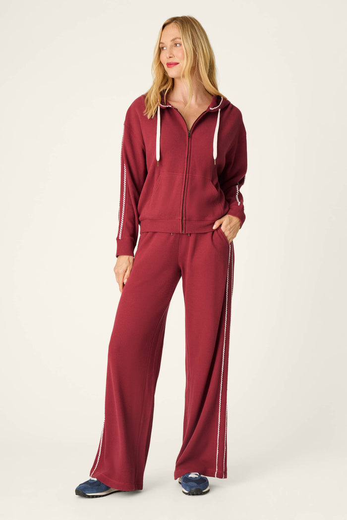 A woman wearing the P.J. Salvage Weekday Waffles Lisette Zip-Up Hoodie and matching wide-leg pants with white stripes stands with one hand in her pocket, smiling, and wearing navy sneakers.