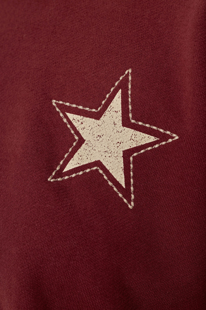 The P.J. Salvage Western Ways Dark Wine Simone Sweatshirt features a slightly distressed white star with a stitched border printed on a maroon background, giving it a vintage-inspired look.