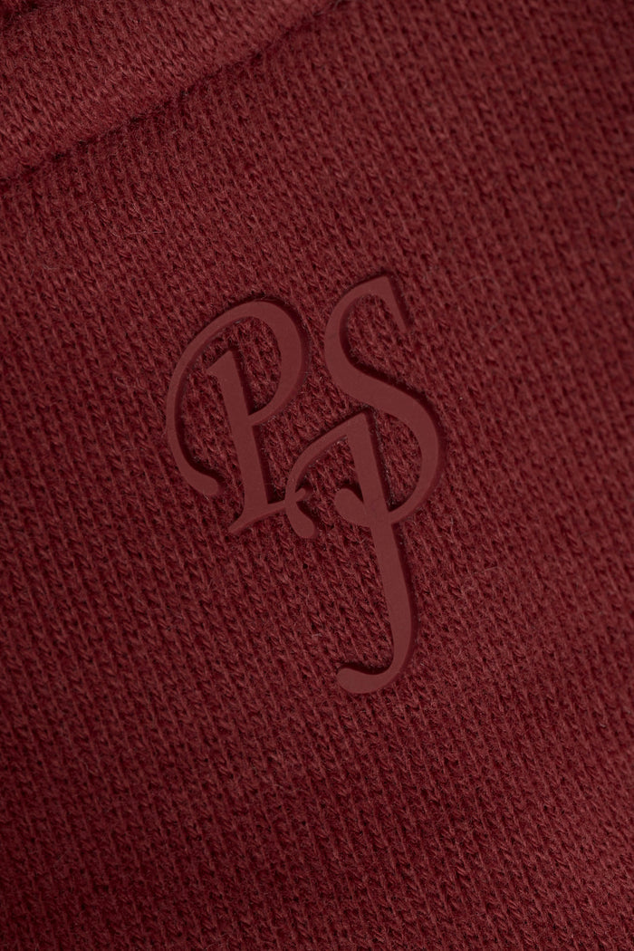 Close-up of textured dark wine fabric featuring embossed overlapping “PS” letters in a stylized serif font.