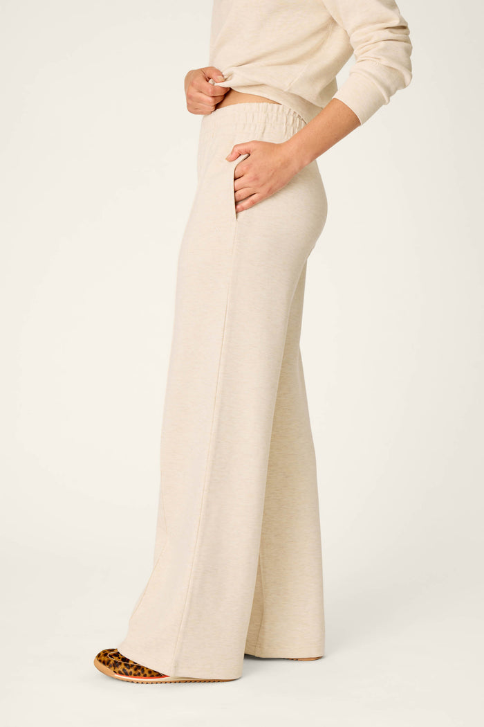 Wearing the P.J. Salvage Western Ways Good Luck Club Runway Lounge Pants, this person is shown from mid-chest down standing sideways. The beige, wide-leg, high-waisted lounge pants feature side pockets and reach the floor, with shoes partially visible beneath the hem.