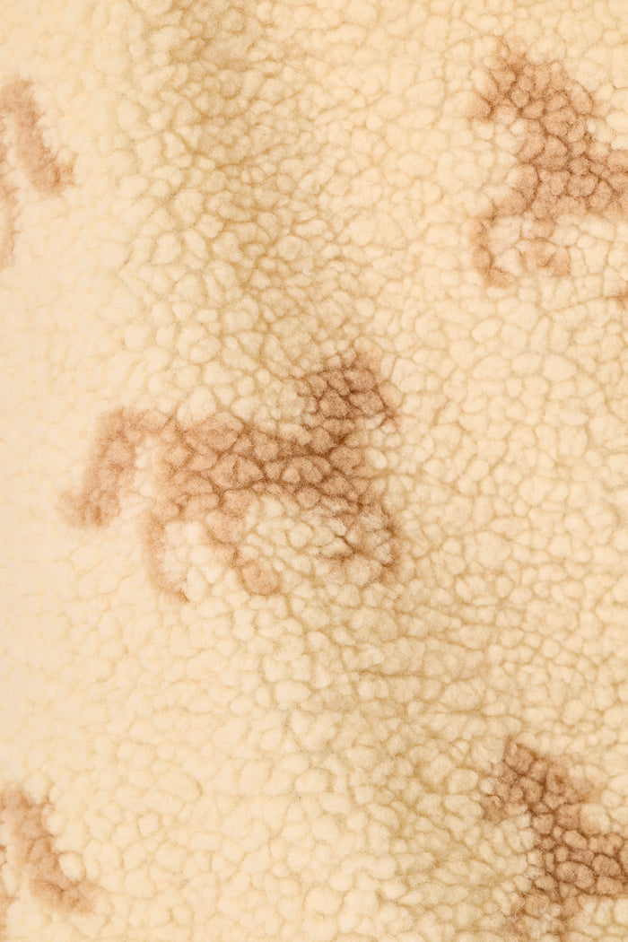 A close-up of a textured cream sherpa fabric with a repeating brown horse pattern.