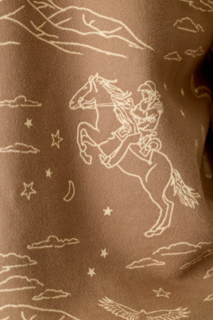 The P.J. Salvage Western Ways Ride ’Em Cowgirl Roll Back Short Sleeve Sweatshirt features a line drawing of a cowgirl on a rearing horse, surrounded by clouds, stars, and a crescent moon, printed on brown fabric.