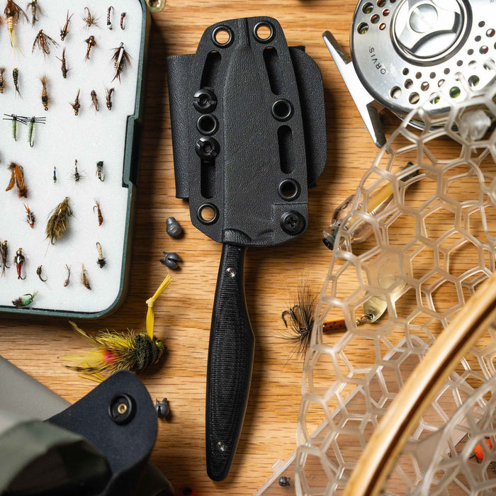 WESTSLOPE black knife with sheath on a wooden surface surrounded by fishing flies and gear. Ideal for outdoor enthusiasts.