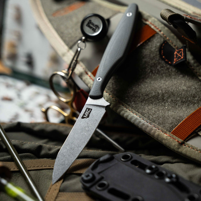 Grey WESTSLOPE knife resting on outdoor gear, showcasing its sleek design and durable blade for outdoor enthusiasts.