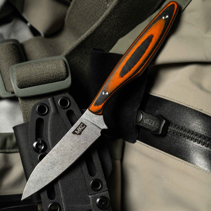 WESTSLOPE knife with an orange and black handle resting on a tactical gear background, showcasing its rugged design.