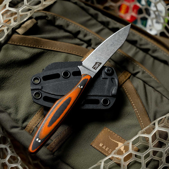 Orange and black WESTSLOPE knife resting on a tactical backpack, showcasing its sleek blade and ergonomic handle.