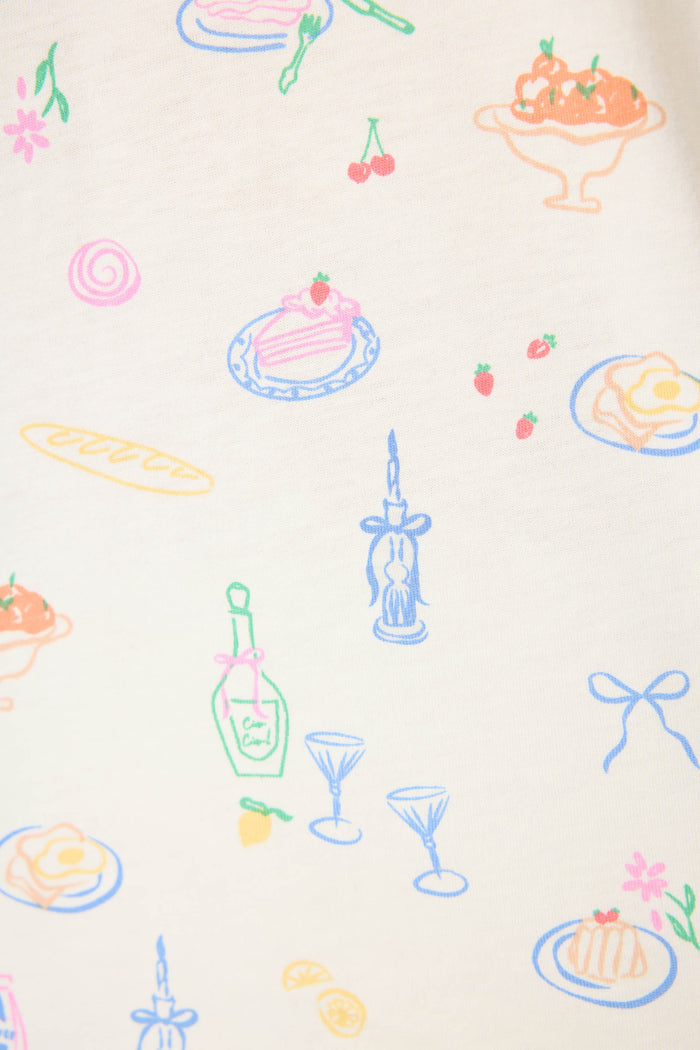 The Whimsy Parisian Picnic Short PJ Set by P.J. Salvage features cream-colored fabric adorned with pastel illustrations of desserts, food, wine bottles, glasses, bread, cherries, strawberries, a bow, and lemon slices.